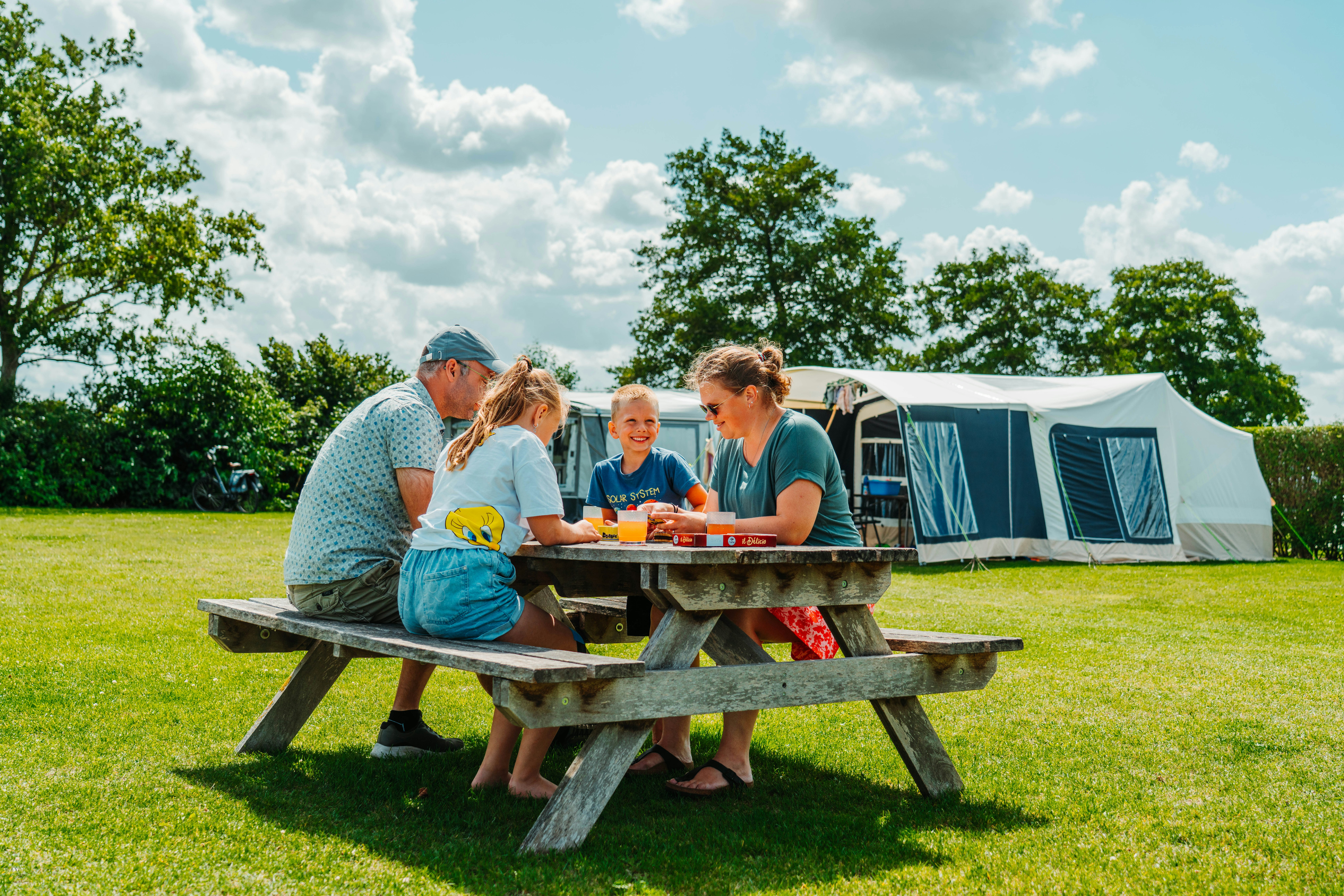 Camping Den Molinshoeve - Familie beim gemeinsamen Essen an einem Picknicktisch auf der Standplatzwiese