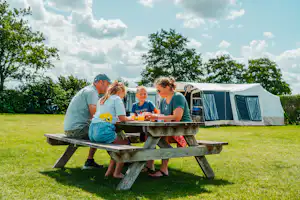 Camping Den Molinshoeve - Familie beim gemeinsamen Essen an einem Picknicktisch auf der Standplatzwiese