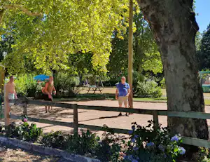 Camping-Terrasse im Grünen mit Blumenbeeten, Schatten spendenden Bäumen und zwei Personen am Weg.