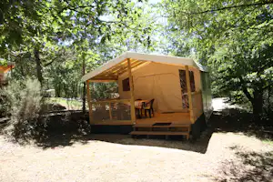 Campingzelt auf Holzterrasse im Grünen, mit Stühlen und Tisch, umgeben von Bäumen im Campingplatzbereich.