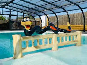 Schwimmbecken mit Poolüberdachung und einer bunten Schwimmfigur auf einer Holzbank am Beckenrand.