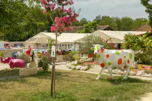 Campinggarten mit Rasen, Zeltzelten im Hintergrund und bunter Dekofigur aus Kunststoff neben einem Kiesweg.