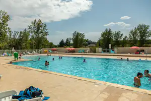 Schwimmbad mit mehreren Gästen im Wasser, Liegen am Rand und Bäumen im Hintergrund vor einem Campinggelände.