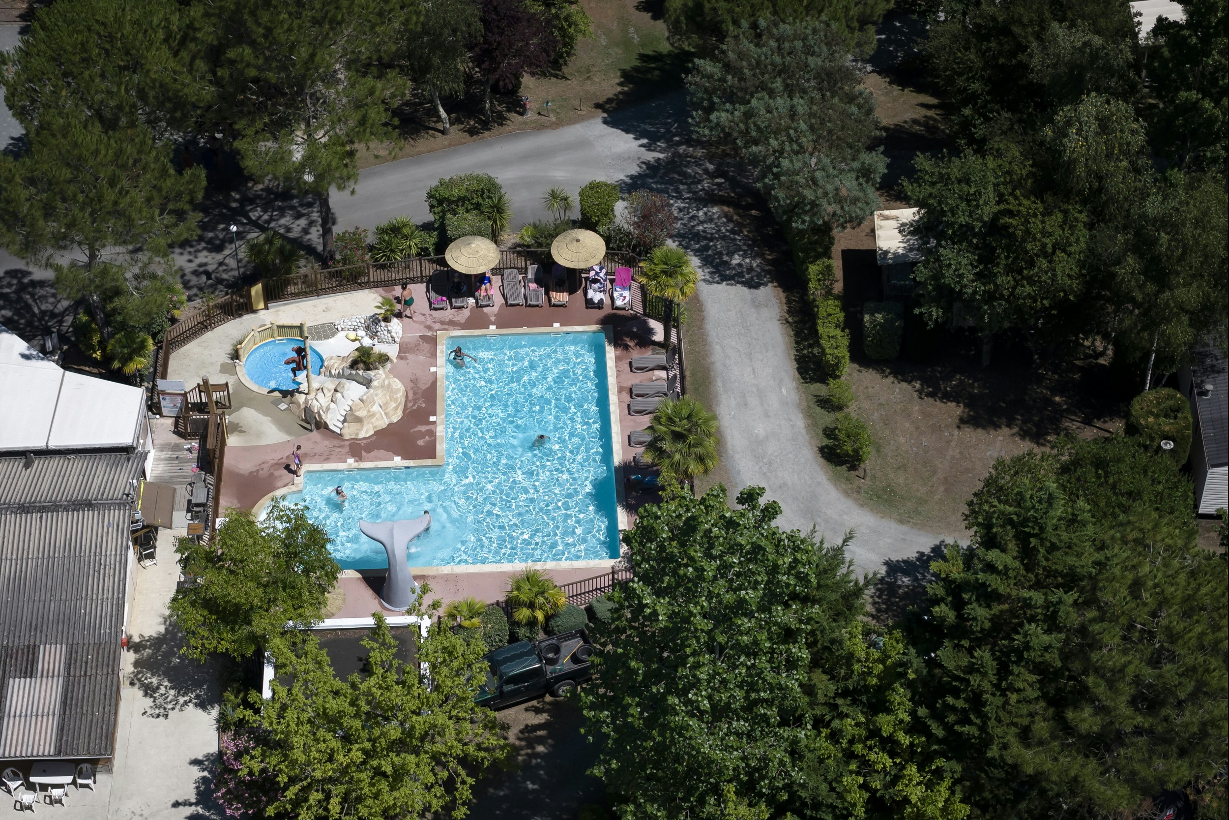 Zwei blaue Swimmingpools mit Liegen am Rand, umgeben von Bäumen und Wegen auf dem Campingplatz.