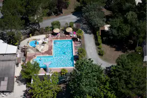 Zwei blaue Swimmingpools mit Liegen am Rand, umgeben von Bäumen und Wegen auf dem Campingplatz.