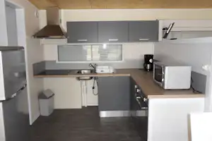 Küchenzeile im Camping-Unterkunftsraum mit Spüle, Herd, Kühlschrank, Kaffeemaschine und Schränken unter Holzdecke.