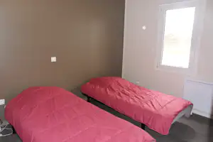 Zwei Betten mit roten Decken, Fenster im Raum und weiße Heizung an der Wand.