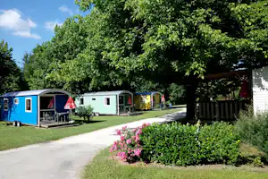 Reihen von Wohnwagen auf einem Campingplatz mit Rasen, Blumenbeeten und schattigen Bäumen entlang eines Weges.