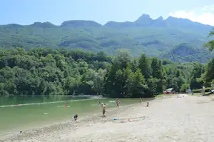 Sandstrand am See mit Badegästen, im Hintergrund Wald und grüne Berge.