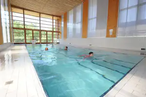 Innenpool mit überdachtem Holz-Deck, großen Fenstern und mehreren Personen im Wasser.