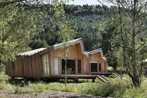 Holzhaus auf einem Campingplatz mit großer Terrasse, großen Fenstern und Blick in den grünen Waldhang.