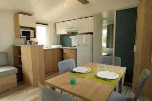 Wohnküche in einem Mobilhome mit Esstisch, Stühlen, Küchenzeile, Mikrowelle und Kühlschrank, Blick durch die Tür.
