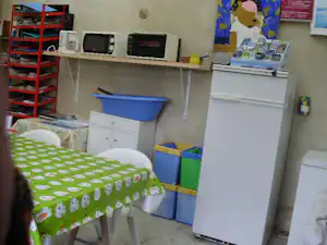 Küchenzeile in einem Camping-Wohnwagen mit Tisch, Stühlen, Regalen und Geschirr, daneben ein blaues und grünes Aufbewahrungsboxen.