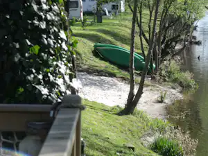 Grüner Schlauchboot am Ufer eines Flusses, daneben Wiese und Bäume, im Vordergrund eine Bank am Campingplatz.