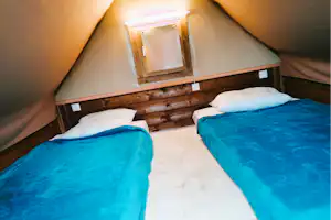 Schlafbereich im Zelt mit zwei Betten, Holzverkleidung und weißen Kissen auf dem Boden.
