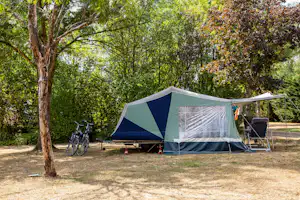 Campingzelt mit Vorzelt auf einem Stellplatz im Grünen, daneben Fahrräder und ein Stuhl am Rand der Bäume.