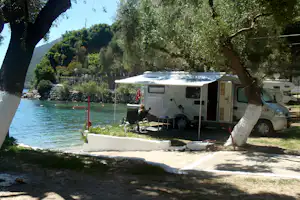 Wohnmobil mit Vorzelt auf dem Campingplatz am See, Sitzgruppe und Bäume im Hintergrund, Berge in der Ferne.