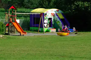 Buntes Familienzelt mit Rutsche und Spielbereich auf dem Campingplatz, daneben ein kleiner Spielturm im Grünen.
