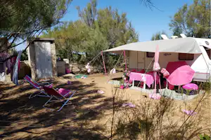 Zelte auf einem Campingplatz zwischen Bäumen, mit Liegestühlen und einem kleinen Tisch im Vordergrund.