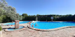 Großes Camping-Schwimmbecken mit Steinmauer, Liegen am Rand und Bäumen im Hintergrund.