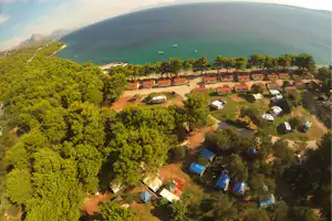 Campingplatz am Meer mit Bungalows, Stellplätzen und vielen Bäumen, Blick auf das türkisfarbene Wasser und Boote.