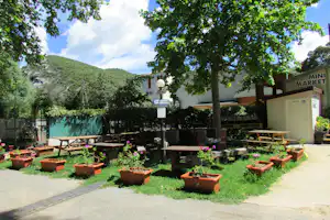 Mini-Market am Campingplatz mit Sitzbänken und Holztischen im Garten, umgeben von Bäumen und grünen Hügeln.