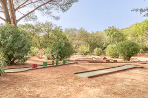 Campingplatz mit Stellplätzen aus Holz und Erde, umgeben von Bäumen und Sträuchern, mit Wegen zwischen den Plätzen.