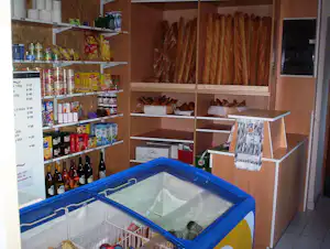 Regale mit Lebensmitteln und Getränken im Camping-Shop, daneben ein blauer Kühlbehälter und eine Theke.