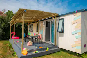 Terrasse am Bungalow mit Pergola, Tisch und Stühlen, Spielzeug auf der Stufe und Rasen neben dem Gebäude.