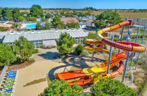 Blick auf einen Campingplatz mit orangefarbenen Wasserrutschen, Spielbereich und Gebäuden im Hintergrund.