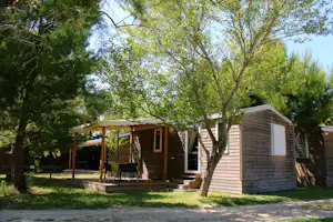 Holzhütte mit Veranda und Sitzgruppe, daneben ein weiteres Holzgebäude, umgeben von Bäumen und Rasen.