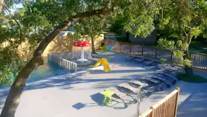 Pool auf der Terrasse mit Sonnenliegen, Sonnenschirm und Zaun, umgeben von Bäumen im Campingbereich.