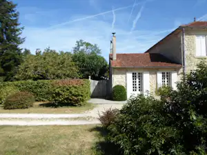 Steinhaus mit rotem Ziegeldach, weißen Fenstern und Terrasse im Grünen, umgeben von Hecken und Rasen.