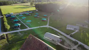 Luftaufnahme eines Campingplatzes mit mehreren Stellplätzen, Wohnwagen und Zelten, Wegen und Grünflächen zwischen Bäumen und Feldern.