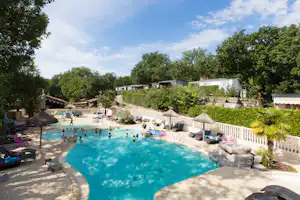 Großes Camping-Schwimmbad mit blauem Wasser, Sonnenliegen und Sonnenschirmen, umgeben von Bäumen und Terrassen.