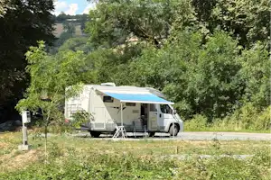 Wohnmobil mit Vorzelt auf einem Campingplatz, umgeben von Bäumen und Grünfläche, mit Tisch und Stühlen am Stellplatz.