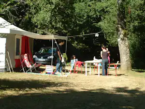 Campingzelt mit rotem Vorhang, Auto davor und Picknicktisch unter Bäumen auf einem Stellplatz.