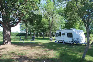Wohnwagen auf einem Campingplatz im Grünen, mit zwei Campingstühlen und Tisch zwischen Bäumen.