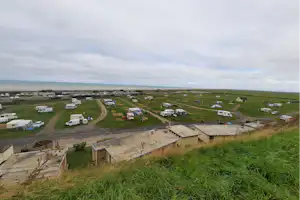 Blick auf einen Campingplatz mit Wohnwagen und Zelten auf grüner Wiese, Feldweg und mehreren Stellplätzen.
