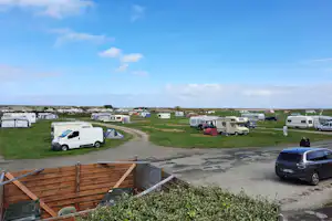 Campingplatz mit Wohnmobilen und Wohnwagen auf grüner Wiese, Schotterweg und geparkten Autos, Blick über den Stellplatz.