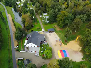 Luftaufnahme eines Campingplatzes mit Wohngebäuden, Stellplätzen, Zufahrtsstraße, Pool und Fluss durch den grünen Park.