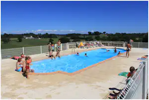 Schwimmbad auf dem Campingplatz mit mehreren Sonnenliegen, Menschen am Beckenrand und Blick auf Wiesen und Bäume.