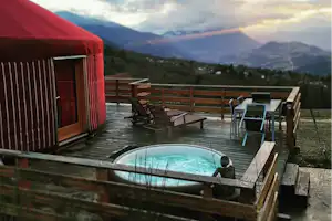 Rote Unterkunft auf einer Holzterrasse mit privatem Pool, Liegen und Blick auf Berge im Hintergrund.