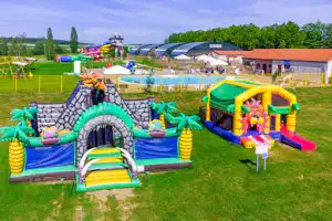 Kinder-Spielplatz mit Hüpfburg und Rutsche auf dem Campingplatz, im Hintergrund Pool, Spielbereich und Gebäude mit roten Dächern.