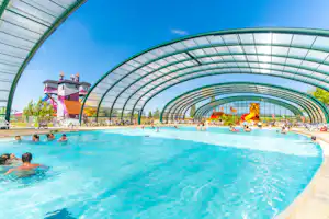 Überdachter Schwimmbadbereich mit blauem Poolwasser, Glasbogen-Dach und mehreren Liegen am Rand.