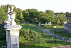 Blick auf einen Campingplatz mit gepflastertem Weg, Rasenflächen, Bäumen und geparktem Auto neben Wohnwagen.