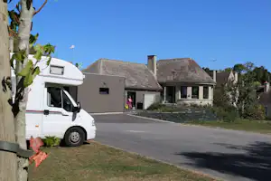 Wohnmobil am Campingplatz neben einem Gebäude mit Satteldach, gepflasterter Zufahrt und Rasenfläche.
