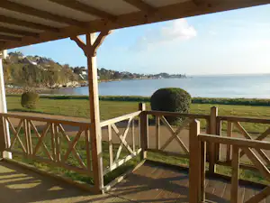Blick vom Holzdeck auf den See, mit Geländer, Rasen und gepflegten Sträuchern am Ufer.