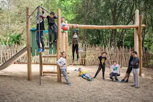 Kinder auf einem Klettergerüst mit Seilen und Schaukeln auf einem Camping-Spielplatz im Grünen, im Hintergrund Bäume.