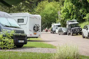 Wohnmobile und Autos stehen auf einem Campingplatzweg, umgeben von Bäumen und Grünfläche.